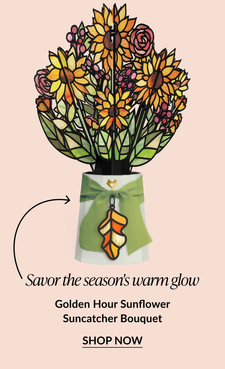 Golden Hour Sunflower Suncatcher Bouquet featuring a vibrant stained-glass style pop-up bouquet with yellow sunflowers and a green ribbon tied around the base, adorned with an autumn leaf charm, and “Shop Now” button.