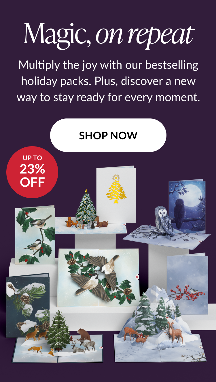 Text on deep purple background reading magic on repeat with description about bestselling holiday value packs and up to 23% off badge above display of pop-up cards featuring winter birds, deer, owls, and Christmas trees with shop now button