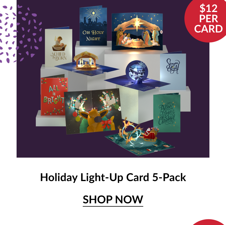 Holiday Light-Up Card 5-Pack featuring illuminated pop-up cards with nativity scenes, Santa’s sleigh, and festive phrases like Oh Holy Night and All Is Bright with red circle noting $12 per card and shop now button