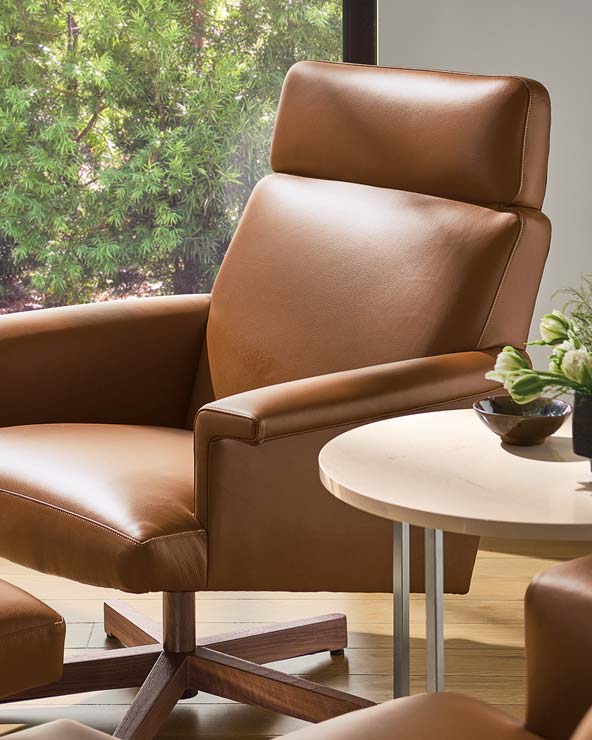 Brown leather recliner with a high backrest, angled next to a round light wood side table with decorative items.