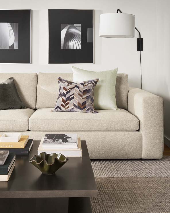 Beige sofa with decorative pillows, paired with a dark wood coffee table featuring a green accent bowl and stacks of books.