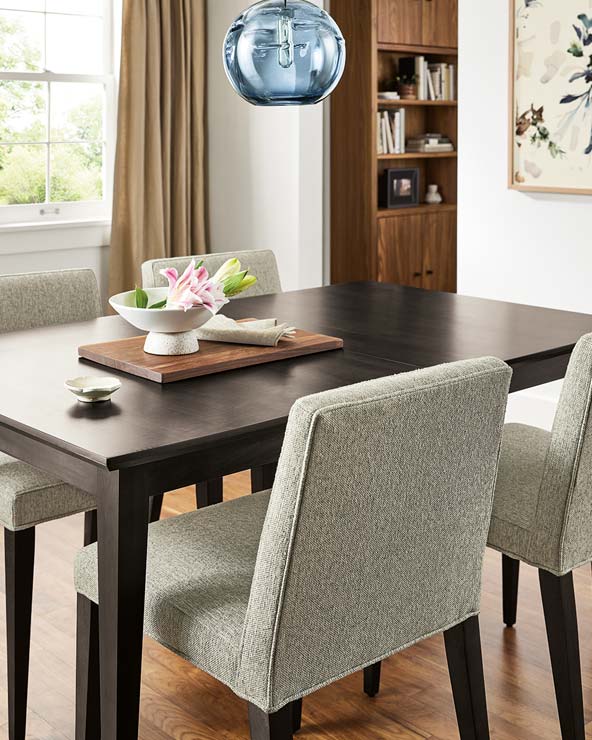 Dark wood dining table with textured light gray upholstered chairs, blue pendant light, and a floral centerpiece.