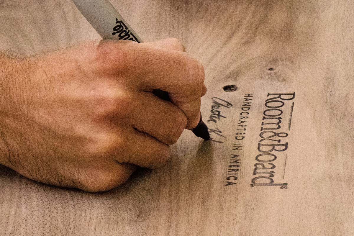 Close-up of an artisan signing Room & Board handcrafted in America stamp on a piece of furniture.