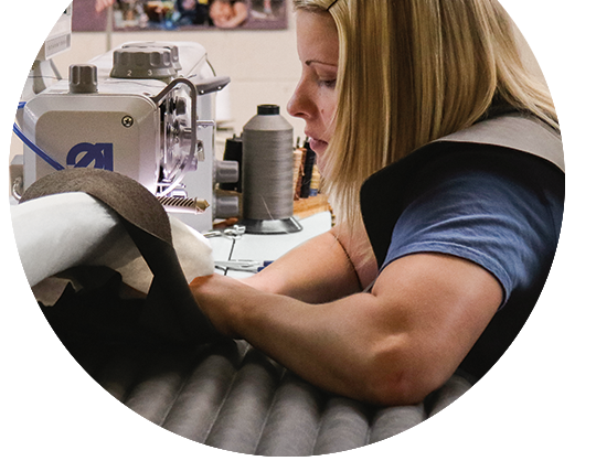 Craftsperson stitching upholstery fabric on sewing machine with spools of thread and materials nearby.