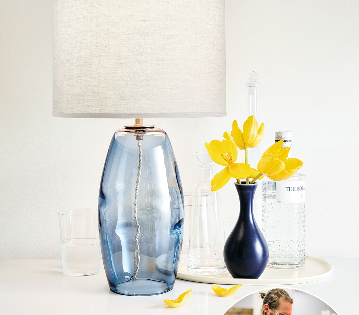 Grace lamp with light fabric shade, blue glass base, and tulip arrangement on bright tabletop.