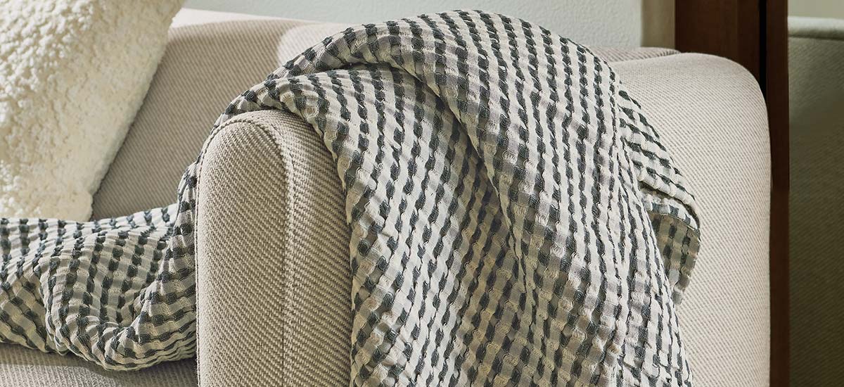 Striped textured throw arranged on beige sofa arm beside ivory accent cushion.