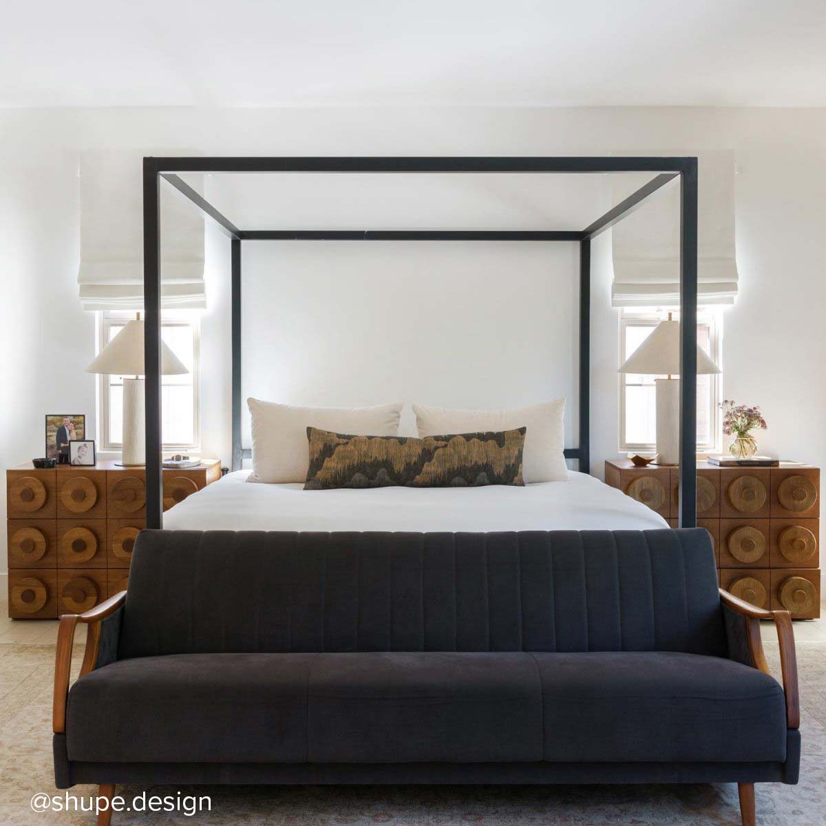 Black canopy bed with white bedding and dark bench in front, flanked by two wood block nightstands.