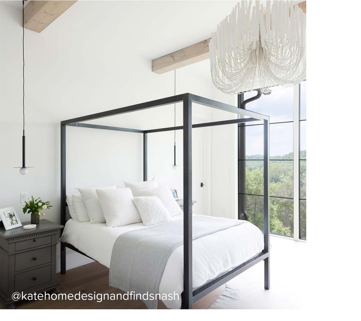 Canopy bed with black frame and grey nightstand, set under exposed beams and chandelier.