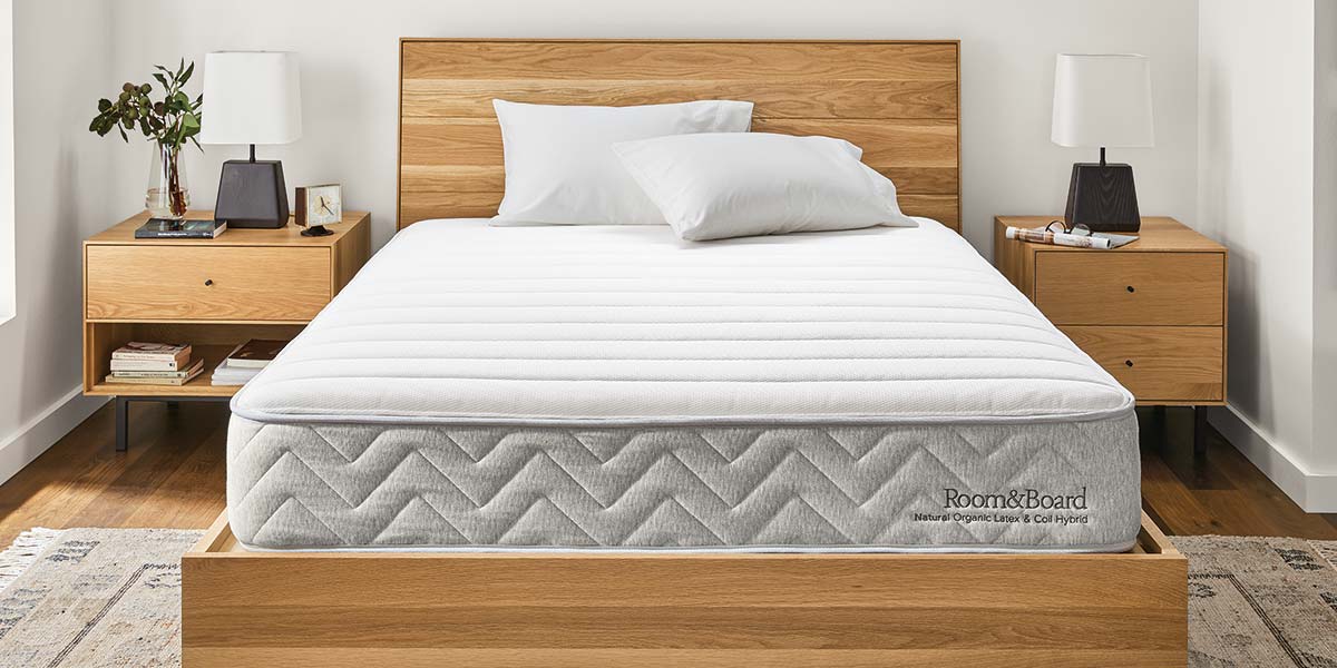 Natural mattress on wooden bed frame with matching nightstands and white lamps, set in a minimalist bedroom.
