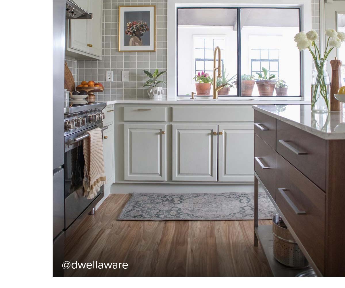 Bright kitchen with grid backsplash, white lower cabinets, wood island, and brass faucet by window.