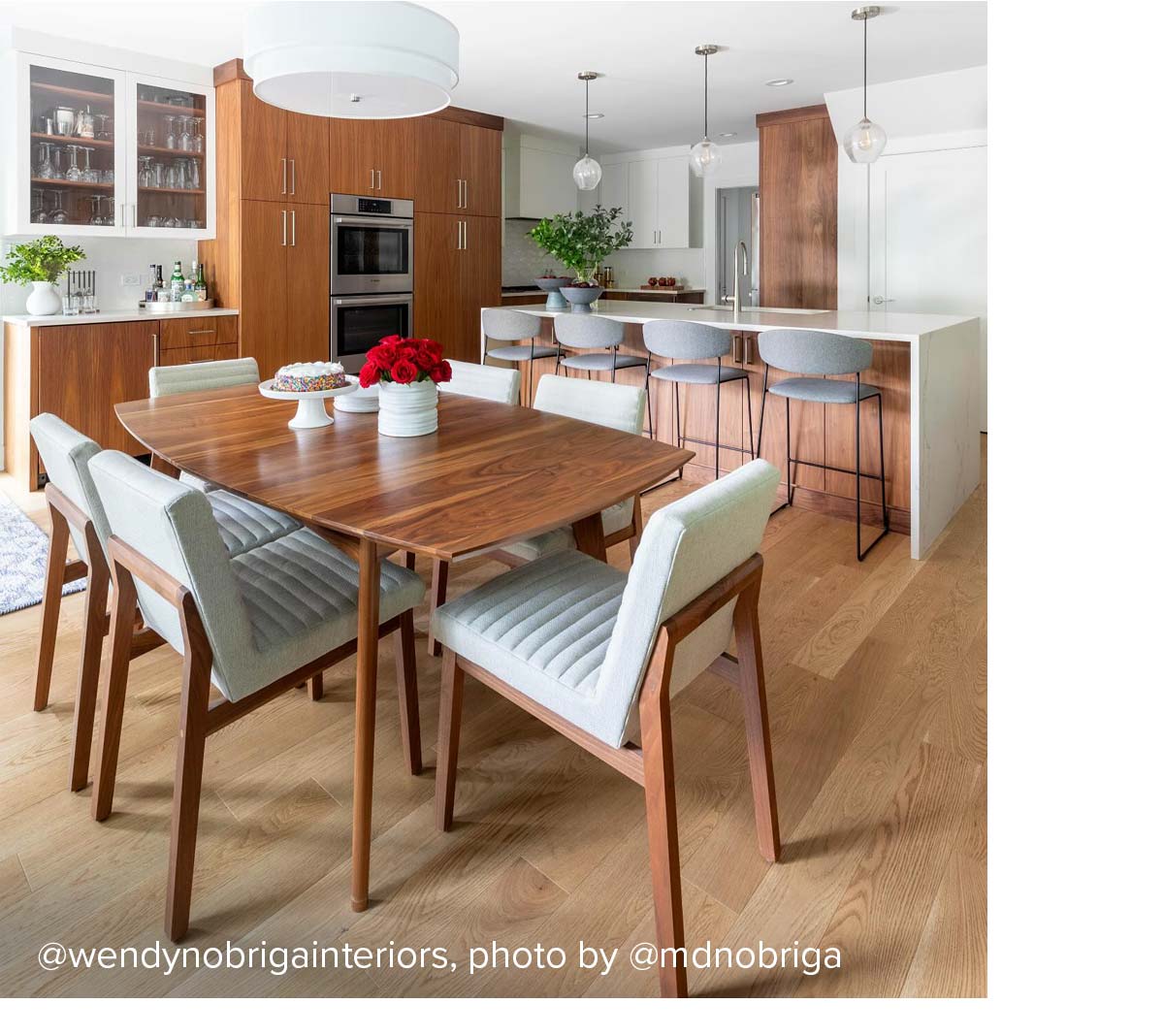 Kitchen with walnut dining table, matching cabinetry, and grey upholstered chairs, with island counter in the background.