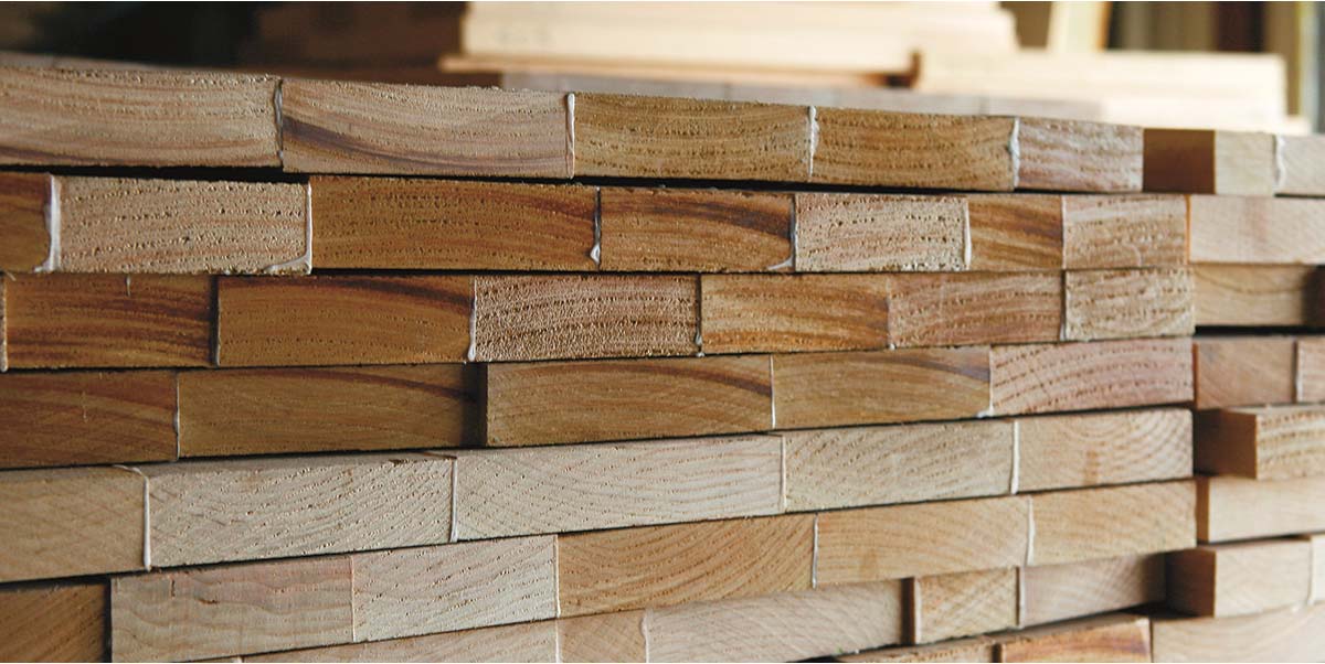 Stack of wood planks in a workshop, showing the grain patterns and varying wood textures.
