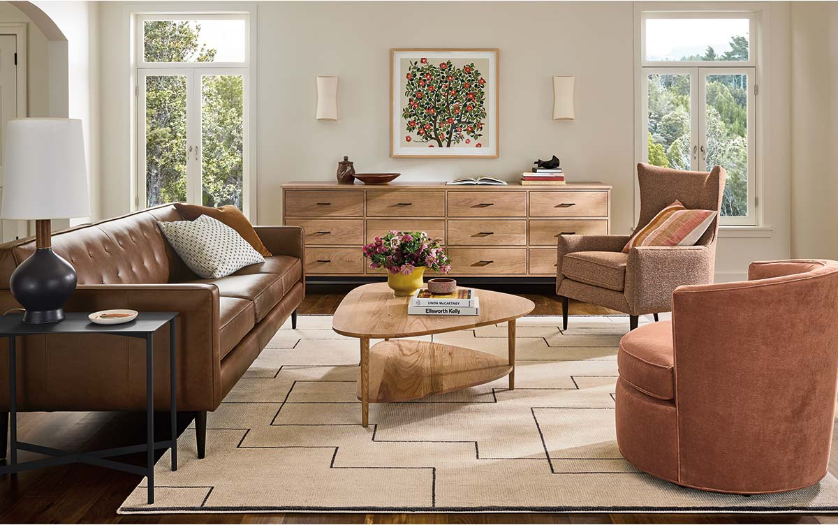 Living room with a leather sofa, two accent chairs, wood dresser and geometric rug.