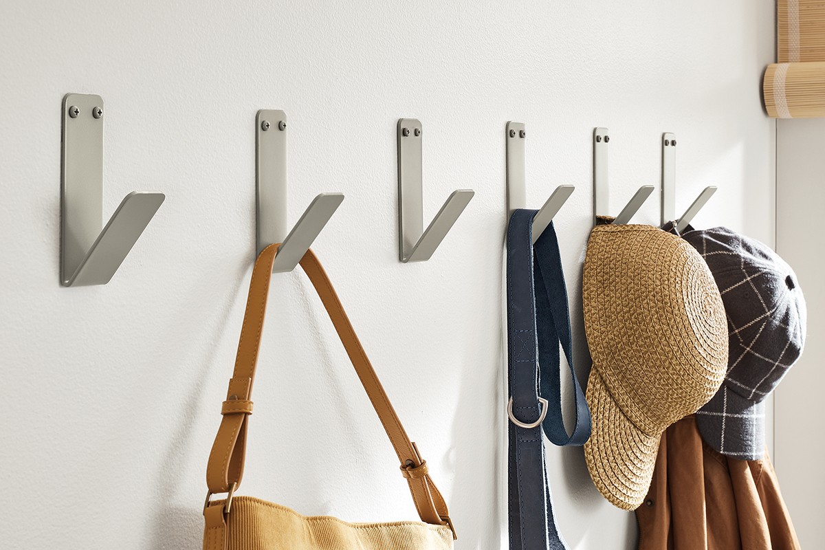 Metal wall hooks with simple angular design, supporting outerwear and bags in a narrow entry hallway.