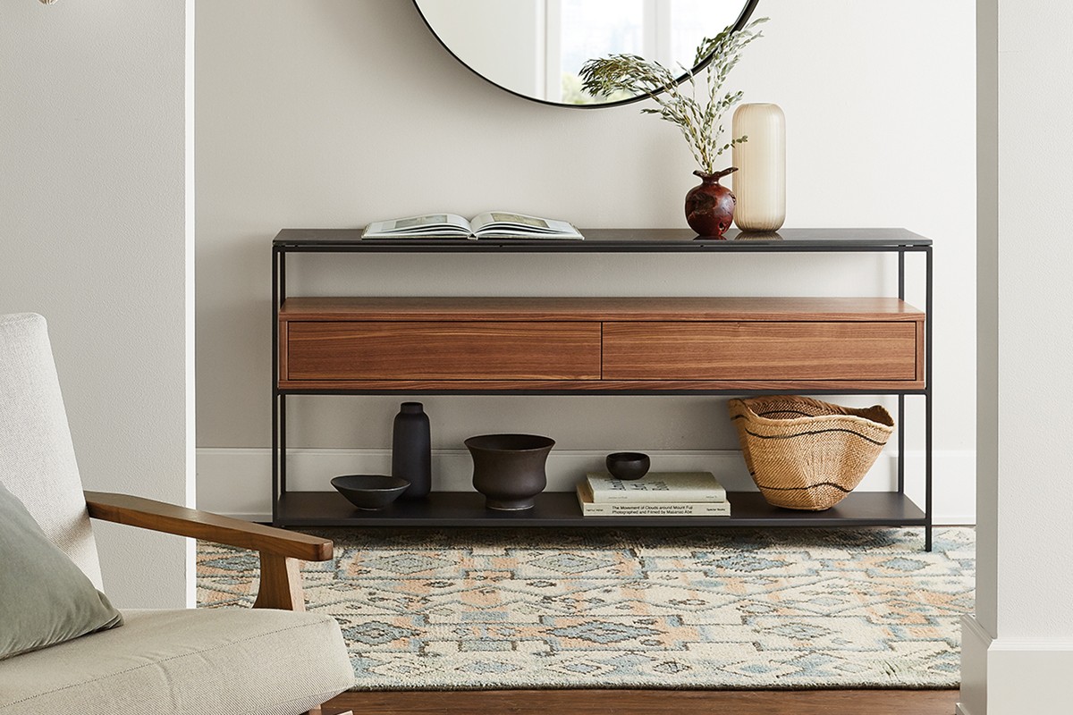 Williams console with black frame and wood drawers, styled with vases, bowls, and books, below a round mirror.