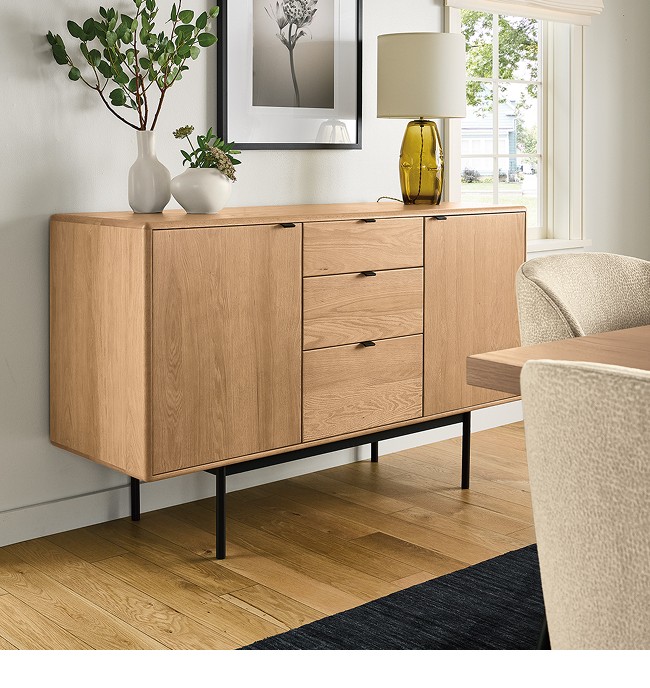 Hensley sideboard with natural wood finish and black handles, placed under framed wall and decor.