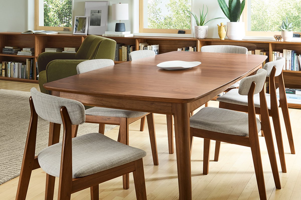 Dining space featuring a Walcott table in walnut, paired with soft neutral chairs and multiple bookshelves lining the walls.