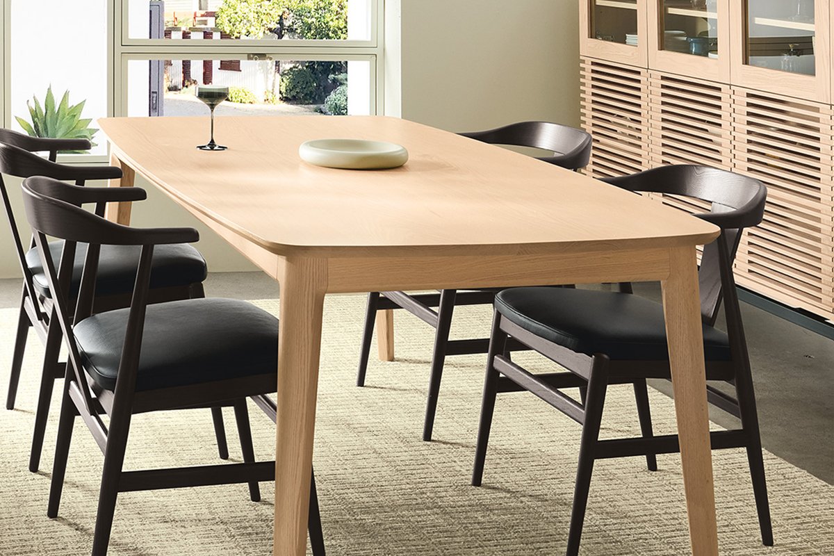 Light oak Walcott dining table paired with four black wood dining chairs featuring curved backs and upholstered black seats.