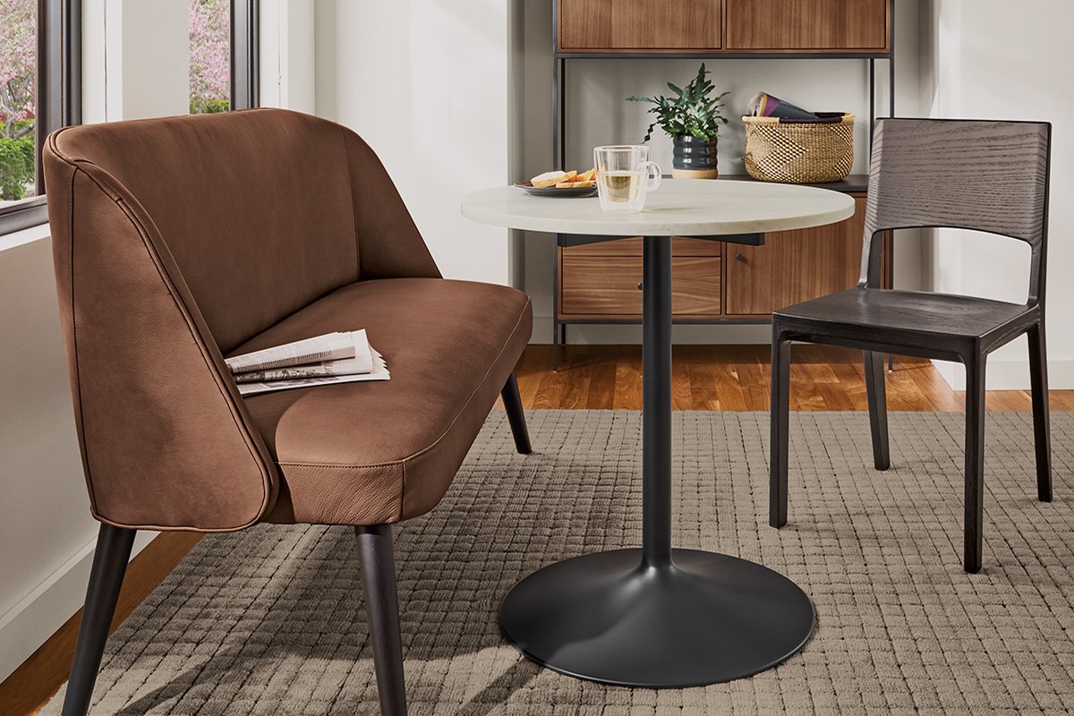 Leather Cora bench with round table and dark side chair on textured grey rug.