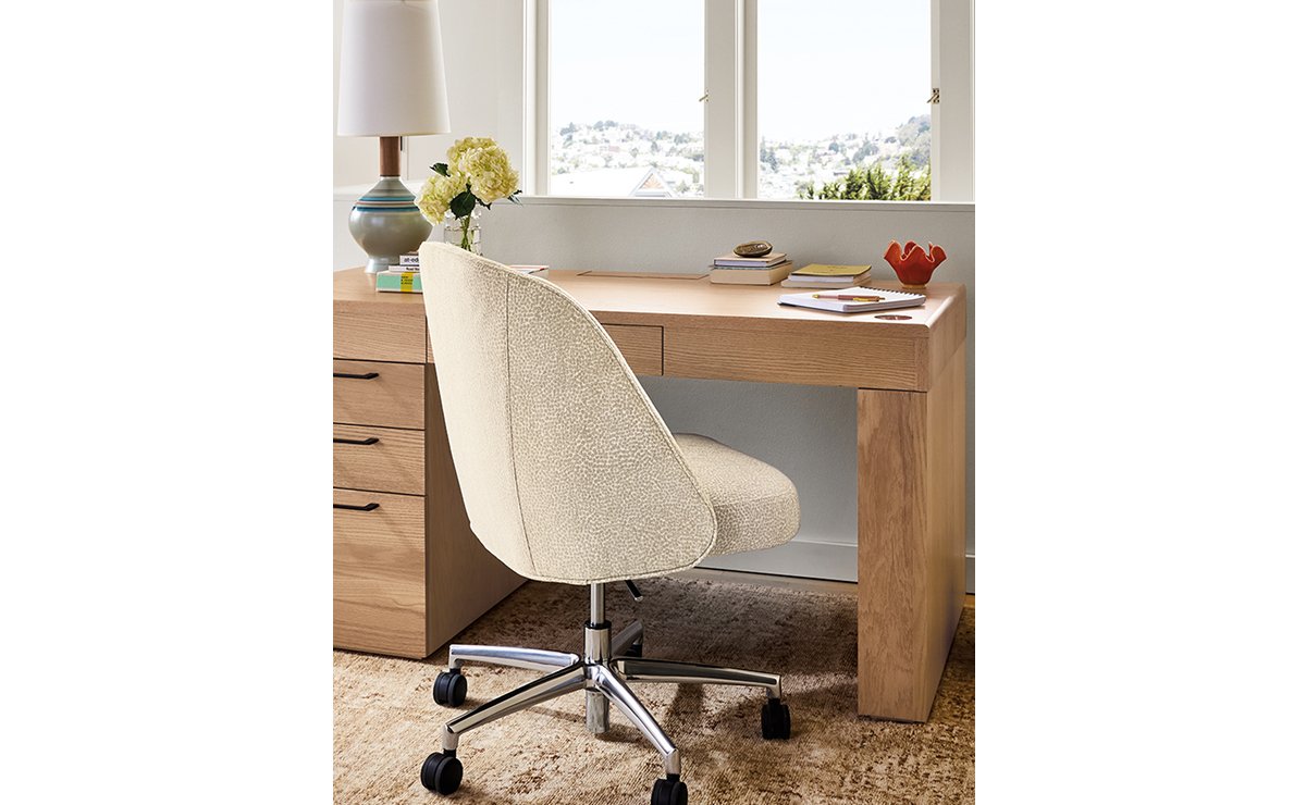 Cream Cora office chair with chrome base at rectangular wood desk with storage drawers.