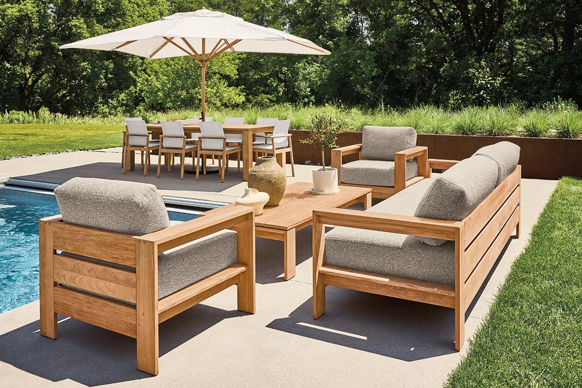 Leti outdoor sofa and chairs with light cushions and teak frames, arranged around a matching coffee table by a pool.