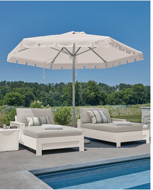 Rayo outdoor chaises with white frames and light cushions beside a pool, shaded by a large patio umbrella.