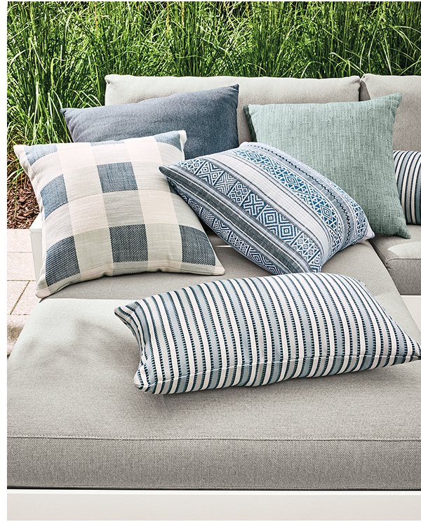 Suki outdoor pillows in plaid, stripe, and blue geometric patterns layered on a light cushion outdoor sofa.