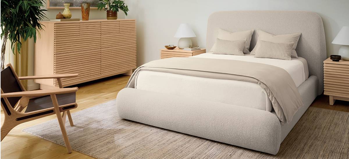 Upholstered bed with rounded headboard and base, flanked by two wood nightstands and a matching dresser.