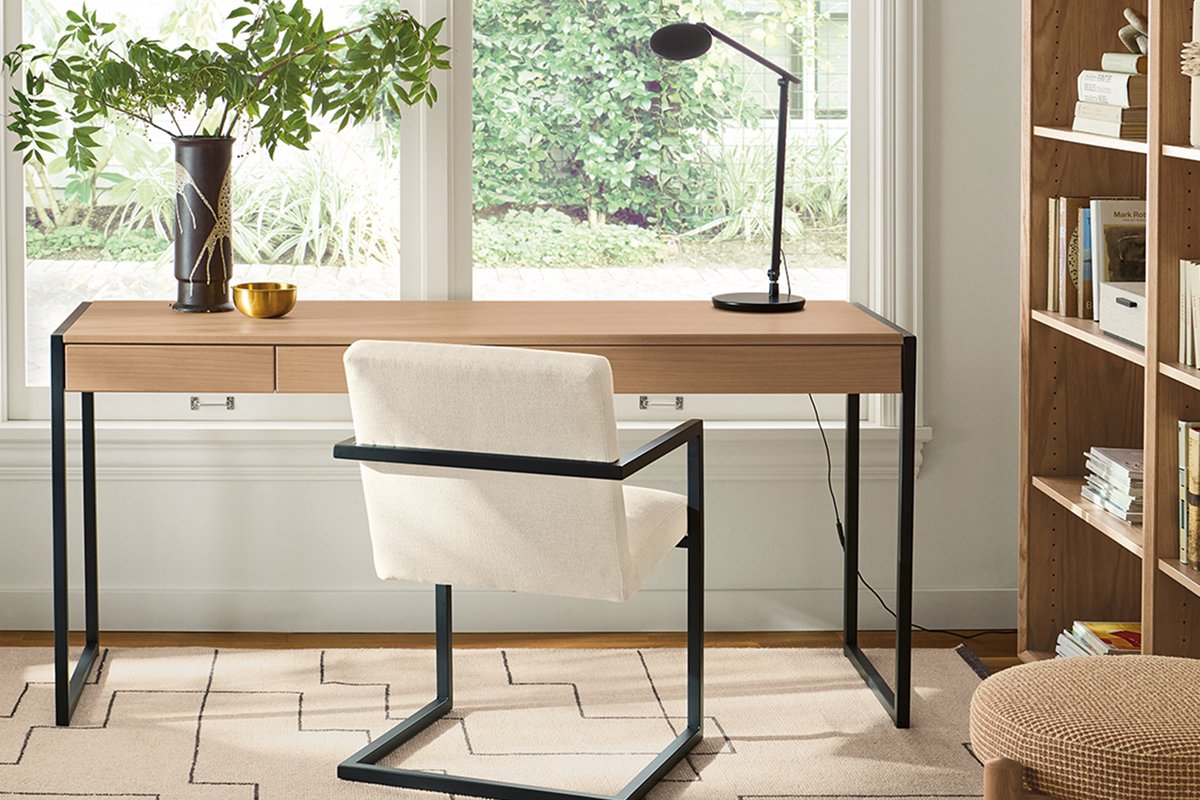 Basis desk with black metal legs and wood top, styled with Lira chair, task lamp, and vase by a window.