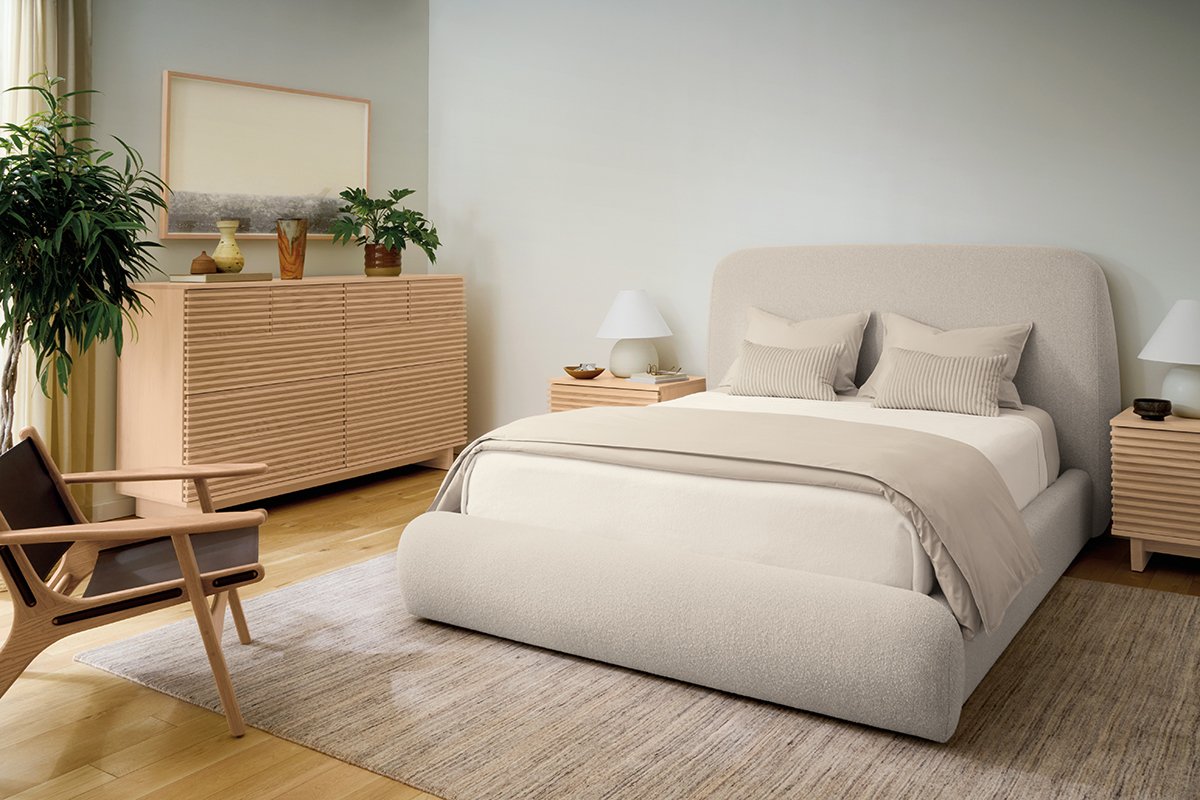 Cream upholstered Luna bed with ribbed wood nightstands and dresser, armchair, and potted plant on neutral rug.