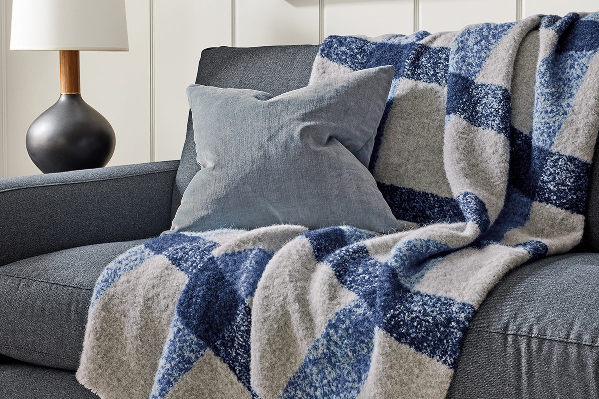 Beaumont throw with blue and ivory check pattern draped over an upholstered sofa with a matching pillow.