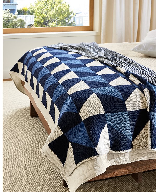 Kepler throw in blue geometric pattern spread across the foot of a bed with light bedding.