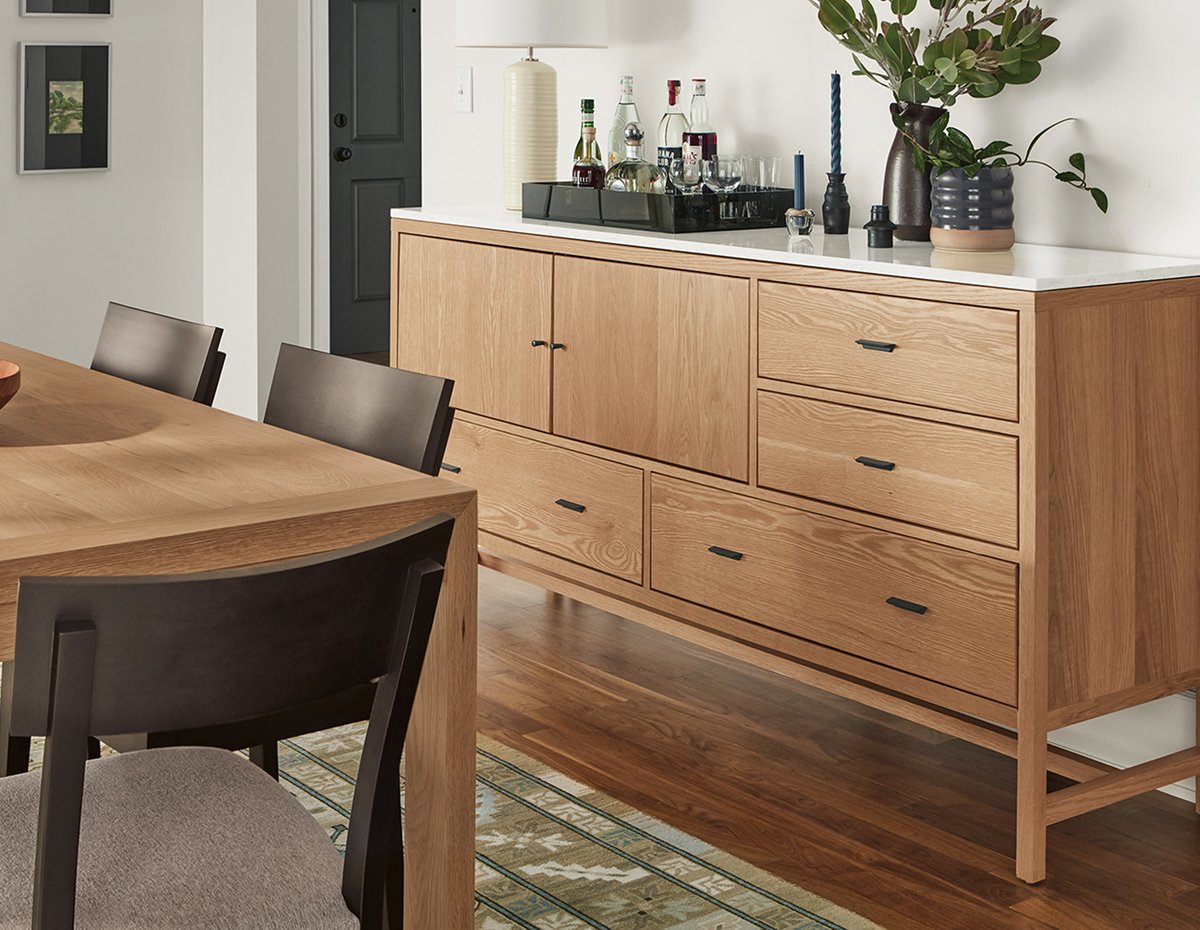 Berkeley storage cabinet with a quartz top, styled with barware and decor, beside a wooden dining table and chairs.