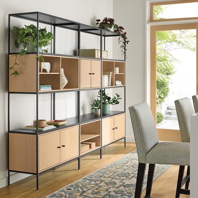 Slim wall unit with wood cabinets and open shelving, styled with plants, books, and decorative items in a bright dining area.