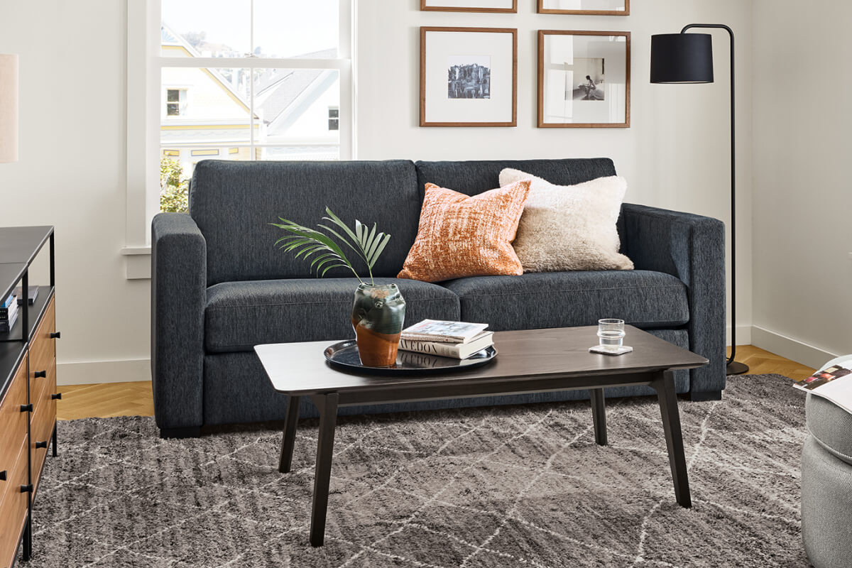Berin sofa in dark fabric with blue and geometric pillows beside black side table and round wood coffee table.