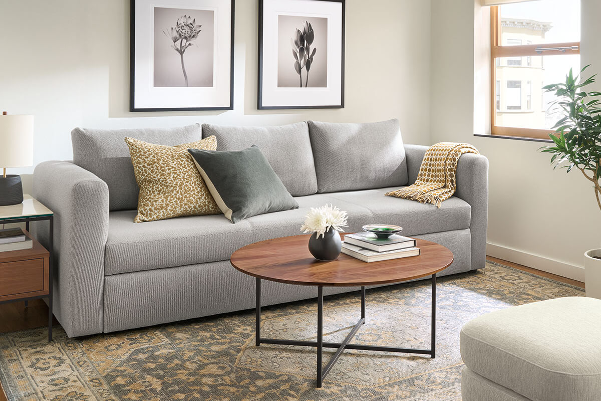 Oxford sofa in light grey with printed pillows and throw, styled with round wood coffee table and wall art.