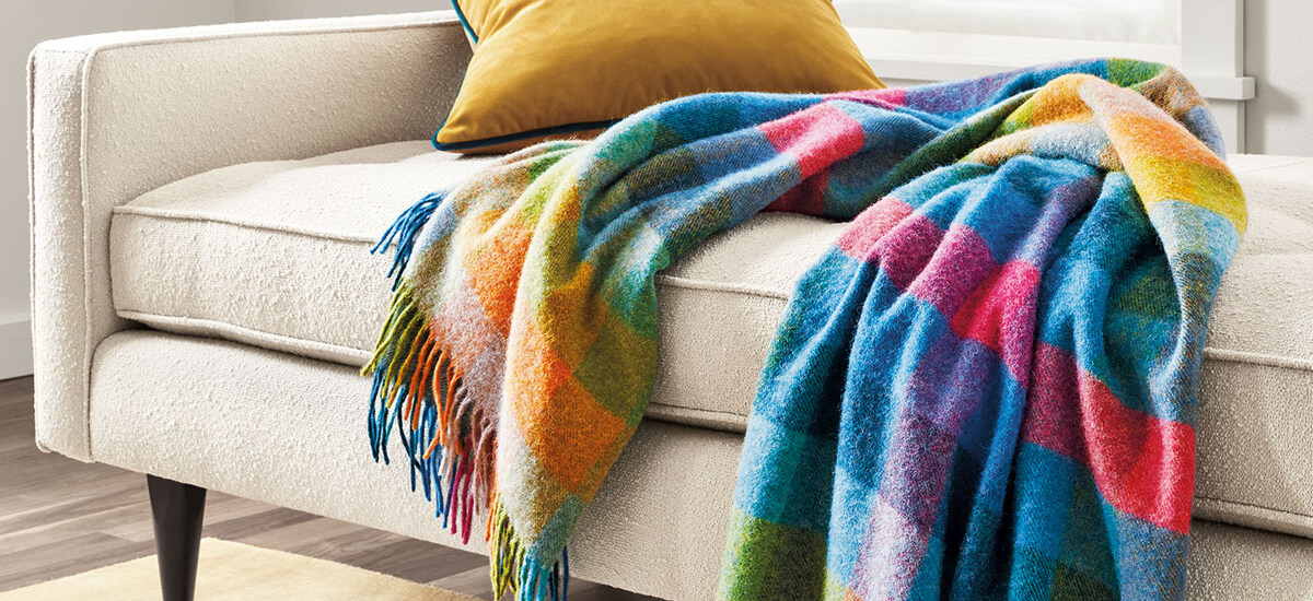 Multicolor plaid throw draped over a cream upholstered sofa with a gold pillow against the back cushion.