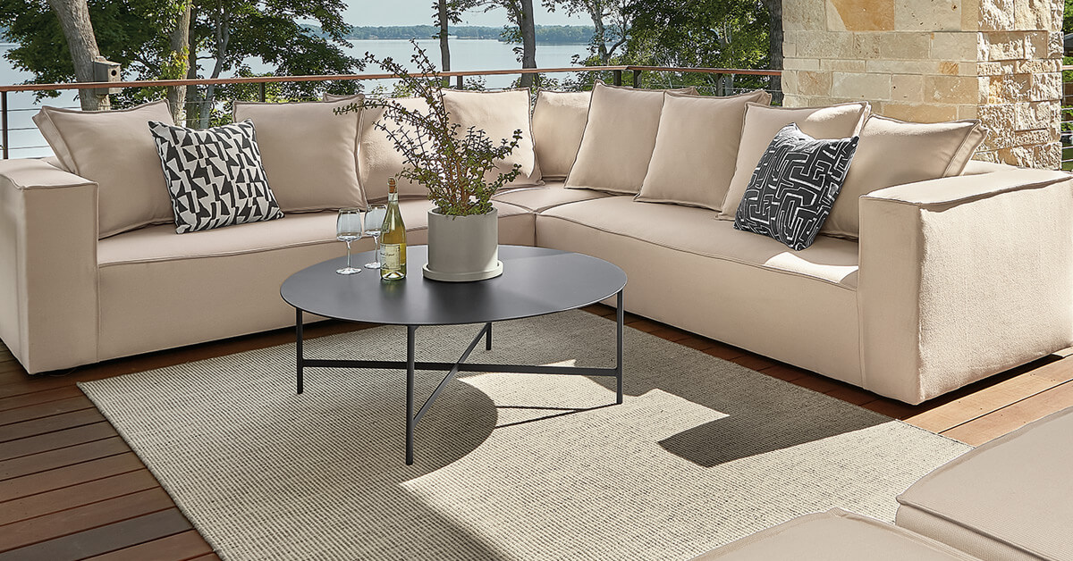 Oasis sectional paired with Selby rug and black coffee table on deck with railing, trees, and water in background.