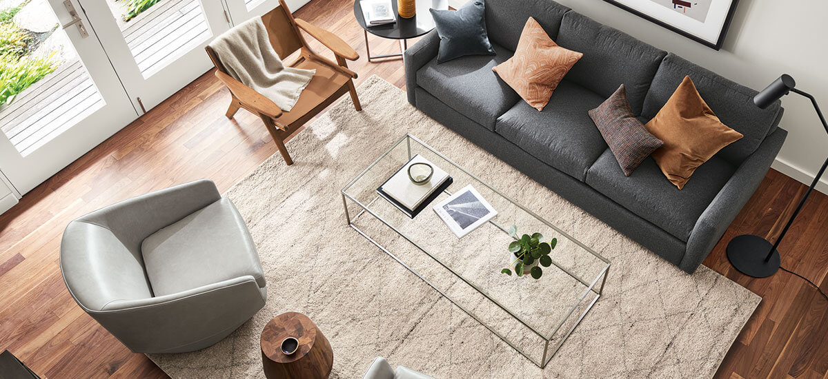 Top-down view of textured Kalindi rug in ivory under modern seating and a clear glass-top coffee table.