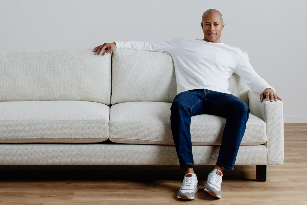 Person seated on a light fabric sofa with their arm resting along the back cushion.
