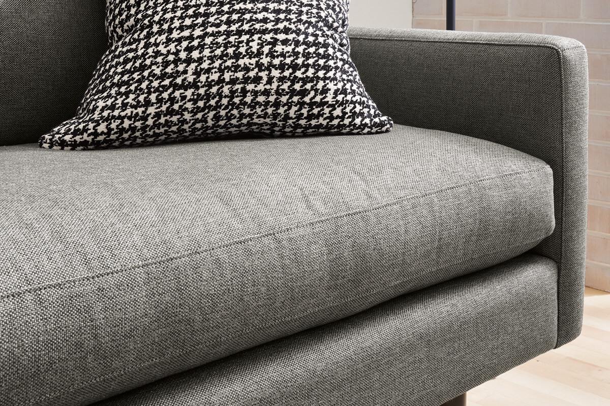 Close-up of a grey sofa seat cushion with a patterned pillow showing textured fabric.