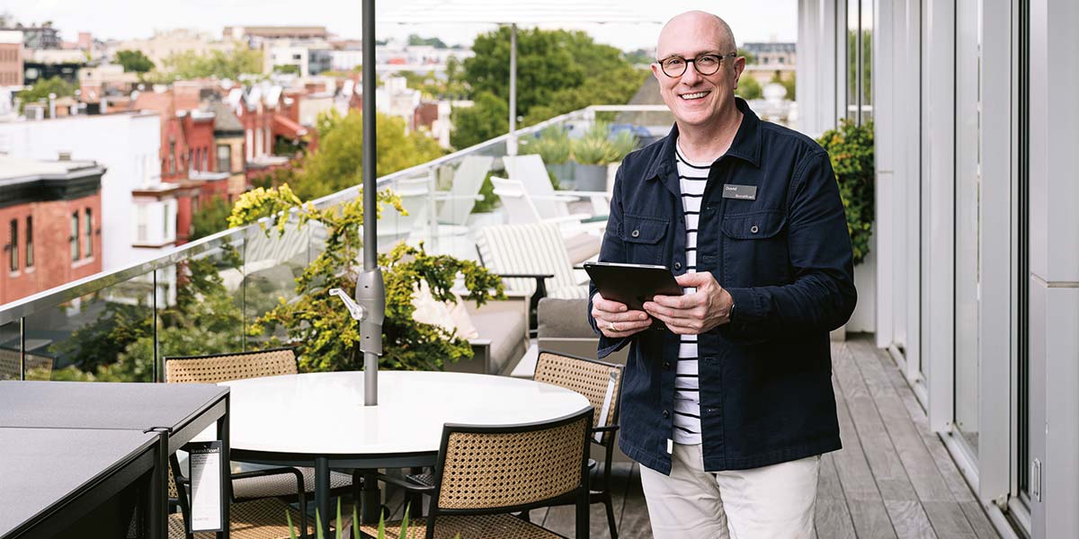 A smiling design associate holding a tablet, standing on a patio next to outdoor furniture.