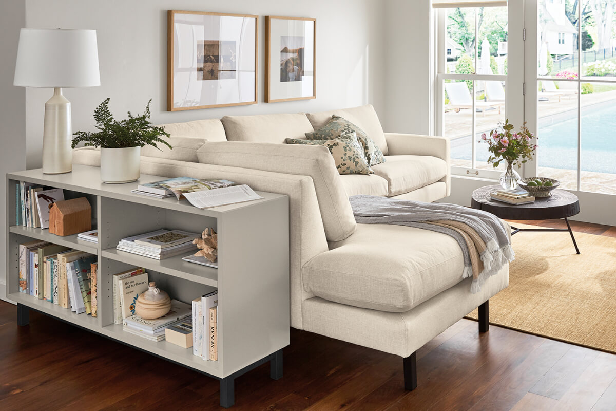 Light upholstered Jasper left arm corner chaise sectional with pillows beside a bookcase console and round table.