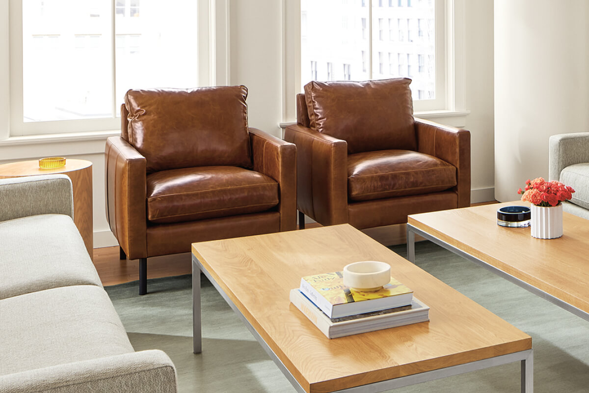 Pair of brown leather Jasper chairs beside a light wood coffee table in a bright living room with large windows.