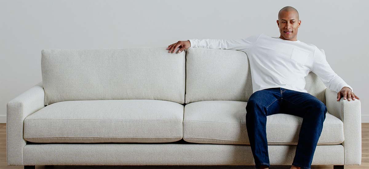 Modern light-tone sofa shown with a person seated with arms draped across the back.