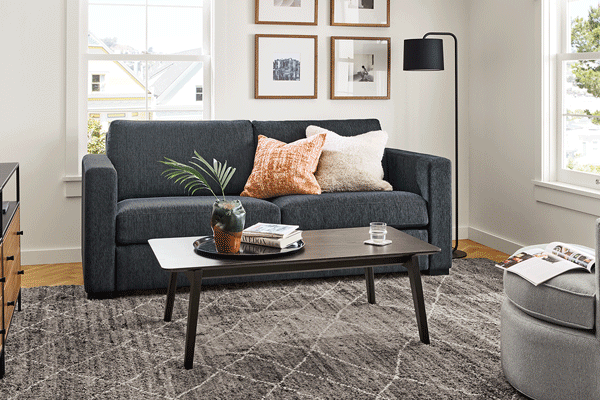 Berin sleeper sofa in dark grey fabric shown transitioning from sofa to bed with pillows and coffee table in a living room.
