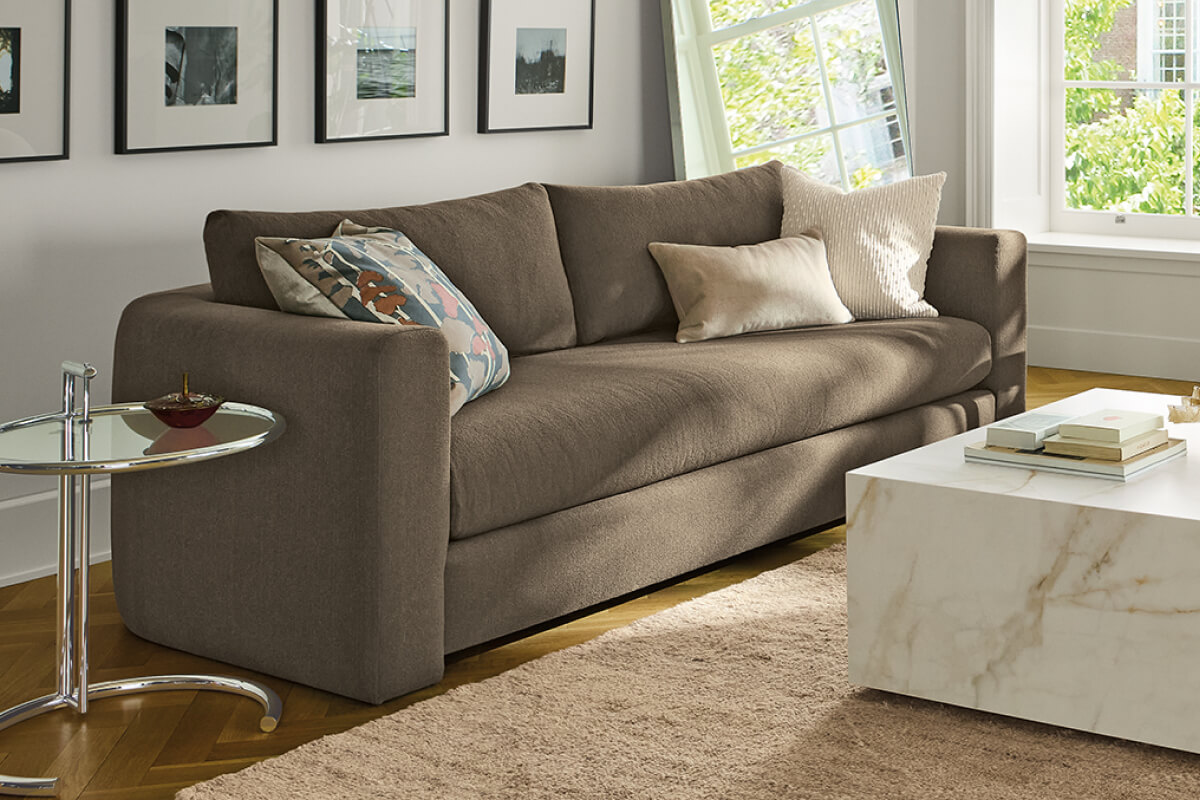 Brown Hannah sofa with accent pillows beside a marble coffee table in a bright living room with framed artwork.