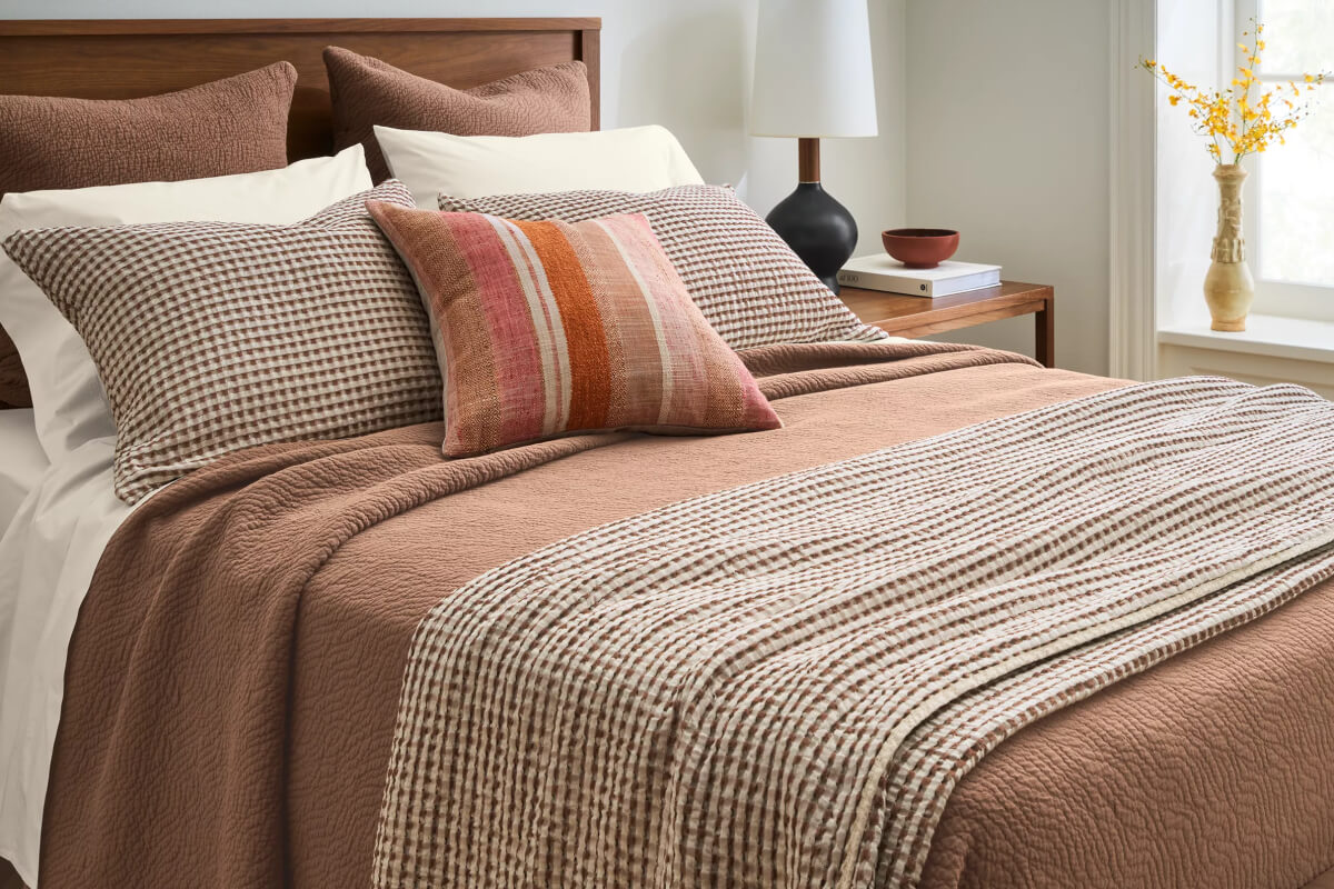 Westin coverlet set with warm-toned bedding and patterned pillows styled on a wood bed with a nightstand and lamp.