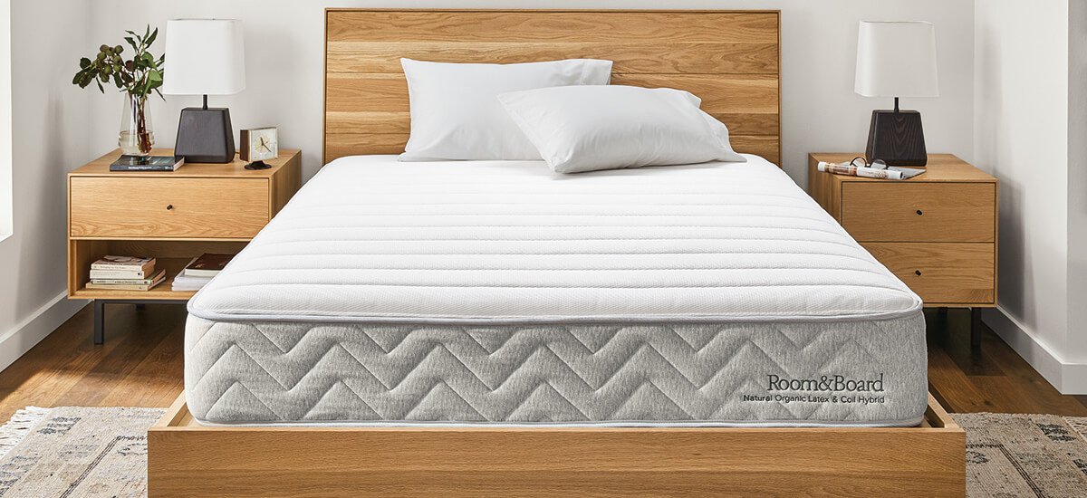 Natural mattress on wooden bed frame with matching nightstands and white lamps, set in a minimalist bedroom.