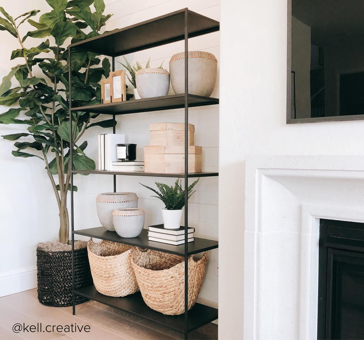 Slim bookcase with black metal frame styled with baskets, books, planters and decor beside a tall plant.